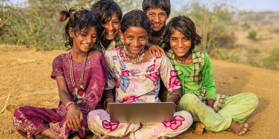 Happy Indian children, sitting on a sand dune and using laptop in desert village, Thar Desert, Rajasthan, India.